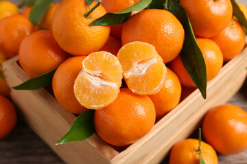 Delicious tangerines with leaves in crate on table, above view