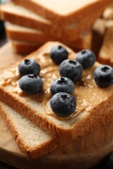 Delicious toasts with peanut butter and blueberries on wooden board, closeup