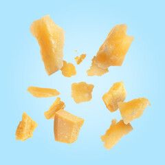 Tasty parmesan cheese falling on light blue background