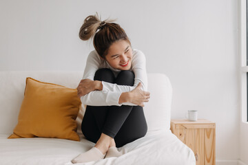 Happy asian woman hug herself on sofa for warmth in good chill winter morning.