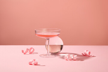 Minimal scene of a glass with modern design filled with pink wine, decorated with a glass ball and...
