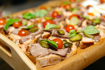 Open-Faced Roast Beef Sandwiches with Fresh Toppings. Delicious open-faced roast beef sandwiches topped with cherry tomatoes, pickles, and basil leaves on a wooden serving board.