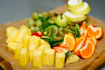 Colorful Fresh Fruit Assortment on Wooden Board. Sliced pineapple, kiwi, strawberries, and green grapes presented on a wooden board for a refreshing and healthy treat.