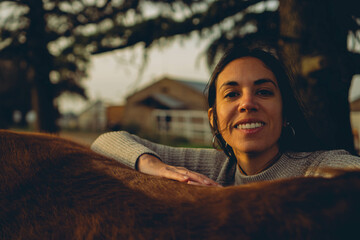 young Latin woman smiles at camera while hugging a horse