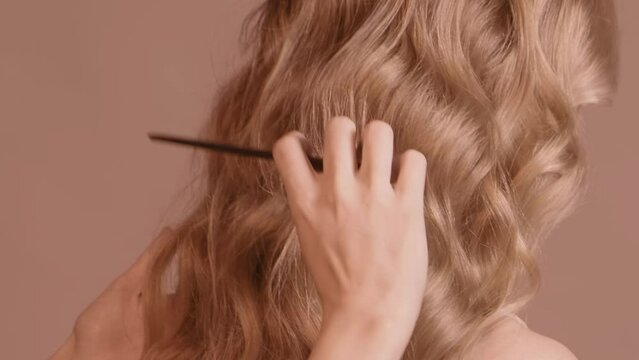 Woman hairdresser combing long wavy ginger female hair from back side.