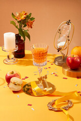 Concept of night party with a wine glass standing on golden dish, displayed with few apples, a candle and a hourglass. A pot of flowers featured