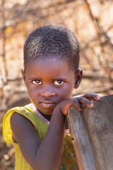 portrait of an african child in the yard ,village life, the girl is holding a wooden chair