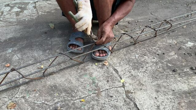 unrecognizable black man hands in white dirty glove tying metal structure using pliers, creating strong iron frame to reinforce concrete construction