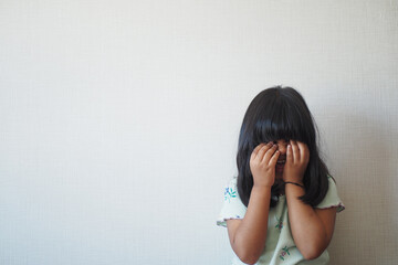 a upset child girl cover her face with hand 