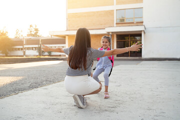 Mother coming to pick up her daughter after school, beautiful sunset image, child runs in her arms