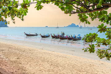 Long-tail boats await passengers at Ao Nang beach. The tourist resort is the starting point for excursions to the Rai Leh beaches in Krabi province - obrazy, fototapety, plakaty