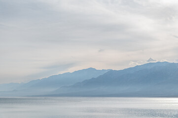 Bluish silhouettes of misty mountains and lake.  Orto-Tokoy reservoir in Kyrgyzstan in winter.