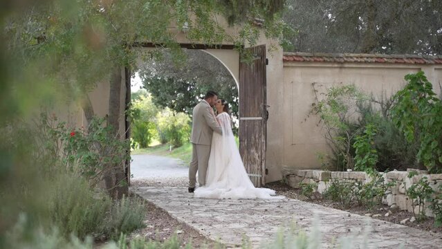 A new bride and groom sneak a kiss under a rustic garden arch doorway.