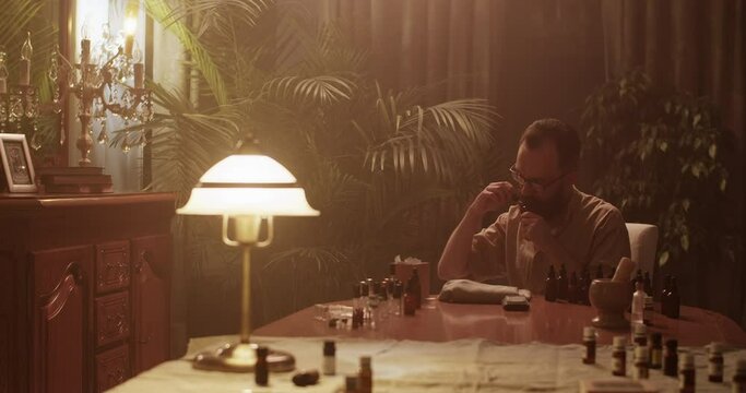Male perfumer smelling oils in dark room while creating perfume