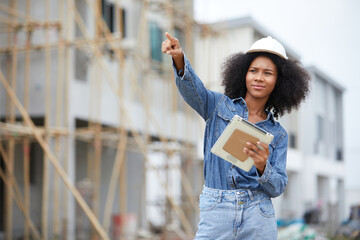African worker or architect holding tablet and pointing to something at construction site