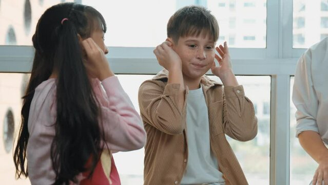 Diverse student learning about body organ while playing with teacher. Multicultural learner sitting around care taker while touching ear in STEM science class. Creative activity concept. Erudition.