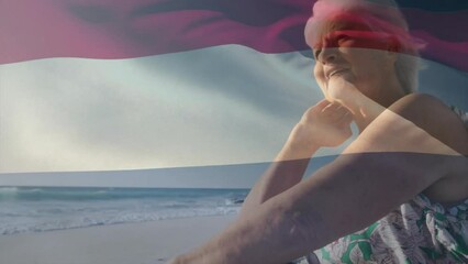 Animation of flag of the netherlands over senior caucasian woman on beach - Powered by Adobe