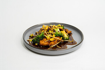 fried Asian dish with sweet and sour sauce, garlic and vegetables on a plate, side view