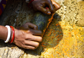 a woman grinding turmeric with a rocky instrument for making ayurvedic or herbal medicine. Selective focus.