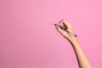 Hand of young woman holding pen on pink background, closeup