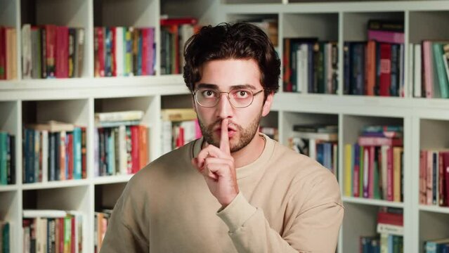 Young man in University Library background. Male showing shush gesture or silent sign closeup.