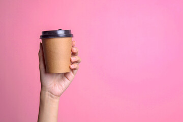 Female hand holding a coffee paper cup mockup isolated on pink background.