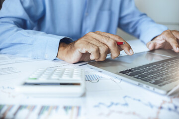 Close-up view, asian businessman using laptop and chart to analyzing and trading stocks online,...