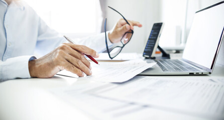 Close-up shot, business consultant holding pen reviewing documents and contact customer via laptop...
