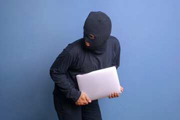 Male thieft with black mask sneaking and stealing notebook computer from the house