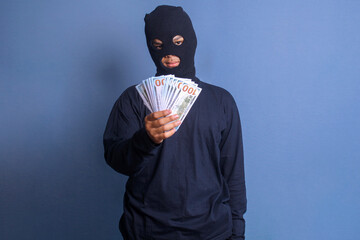 Man wear black mask holding bunch of hundred dollars bills. Burglary, illegal activity and crime...