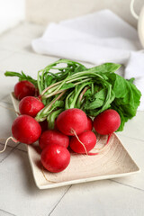 Plate of fresh radishes with leaves on light tile background