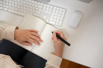 Top view image of a woman is taking notes or writing something in her book at her desk.