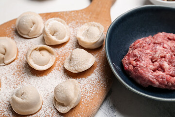 Wooden board with uncooked dumplings and minced meat on table