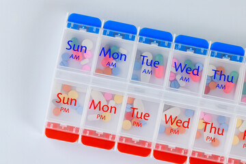 Organizer daily pill dispenser box with medications capsules on white isolated background.