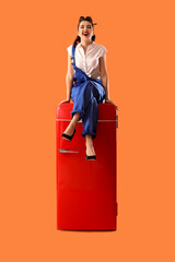 Attractive pin-up worker sitting on retro fridge against orange background