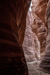 A small  shallow stream flows between high rocks with intricate natural patterns on their walls along walking trail in Wadi Numeira gorge in Jordan