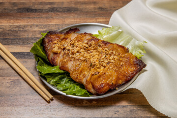 Grilled Pork Jowl steak with lettuce leaf and chopsticks served in dish isolated on wooden table top view of hong kong fast food