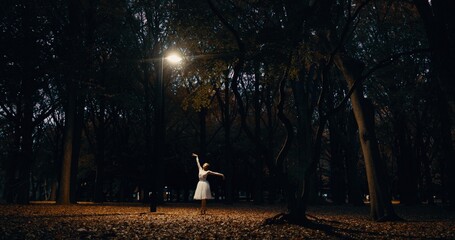 Ballet, dance and woman outdoor at night in Japan with street light, trees and creative art. Ballerina, performance and talent in dark Kyoto forest, woods or garden with spotlight in nature or park