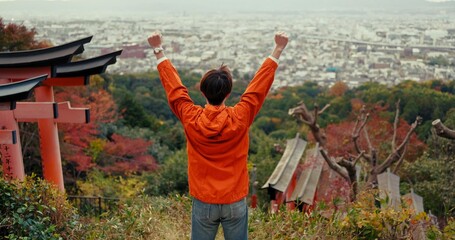 Man, fist celebration and mountain with view, city and torii gates at Fushimi Inari shrine for...