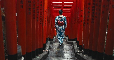 Woman, shinto religion and walk by gates in japan, spiritual path and indigenous culture in kimono. Person, traditional clothes or worship in peace, respect or beauty by Fushimi Inari Taisha in kyoto - obrazy, fototapety, plakaty