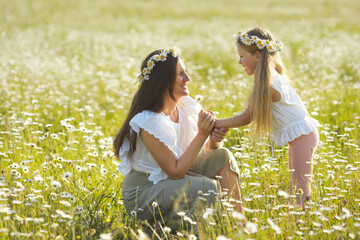 Lifestyle mother and little child in cotton casual clothes playing together in chamomile field. Mom...
