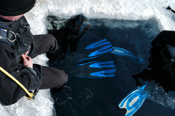Divers sitting at the edge of an ice hole, equipped to immerse