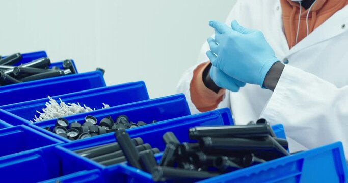 Black lab technician in lab jacket and blue gloves packs cannabis pre-rolls into a tube that will be sold in dispensaries. Medium shot. SLOW MOTION