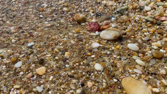 Waves hitting beautiful colourful natural stones rocks sand in sea water at the beach in Cavalière Lavandou South of France, nature holiday vacation, 4K static shot