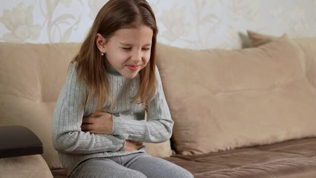 Girl with abdominal pain sitting on a sofa and holds her stomach