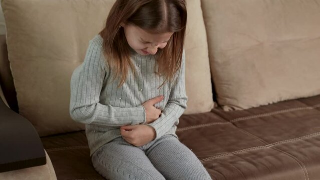 Girl with abdominal pain sitting on a sofa and holds her stomach