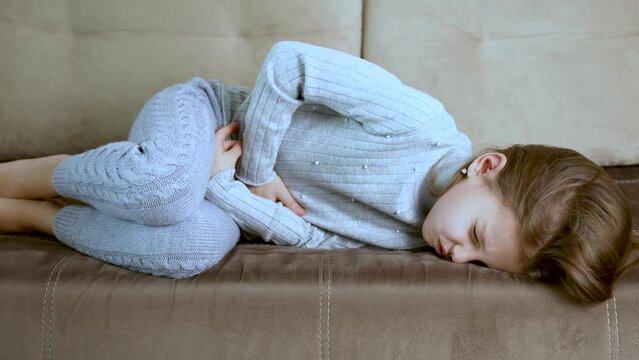 Little girl lying on a sofa and holds her stomach