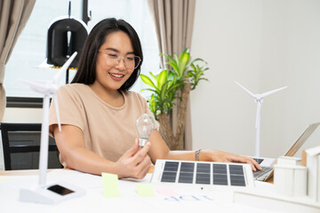 Portrait of young Asian woman working with solar light bulb and computer at home.