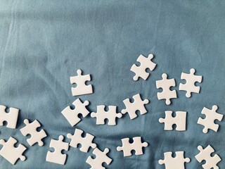all-white jigsaw puzzle pieces on a green-blue fabric background with copy space on the top of the frame