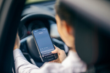 Selective focus on hand typing a message while a woman driving a car.